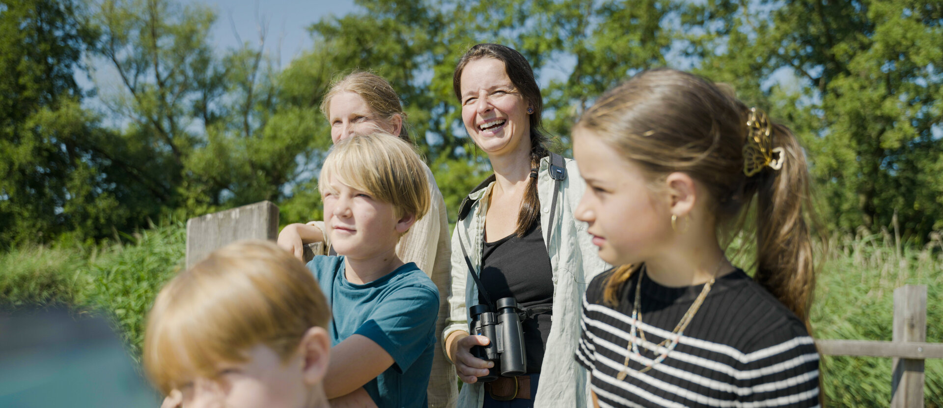 Two women and three children stand on a parapet and gaze into the distance. One of the women smiles and wears binoculars around her neck.